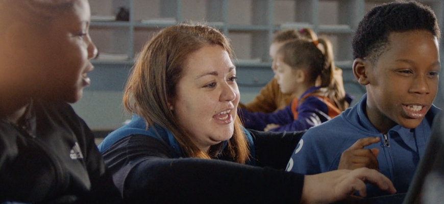 A teacher helps two students in class.